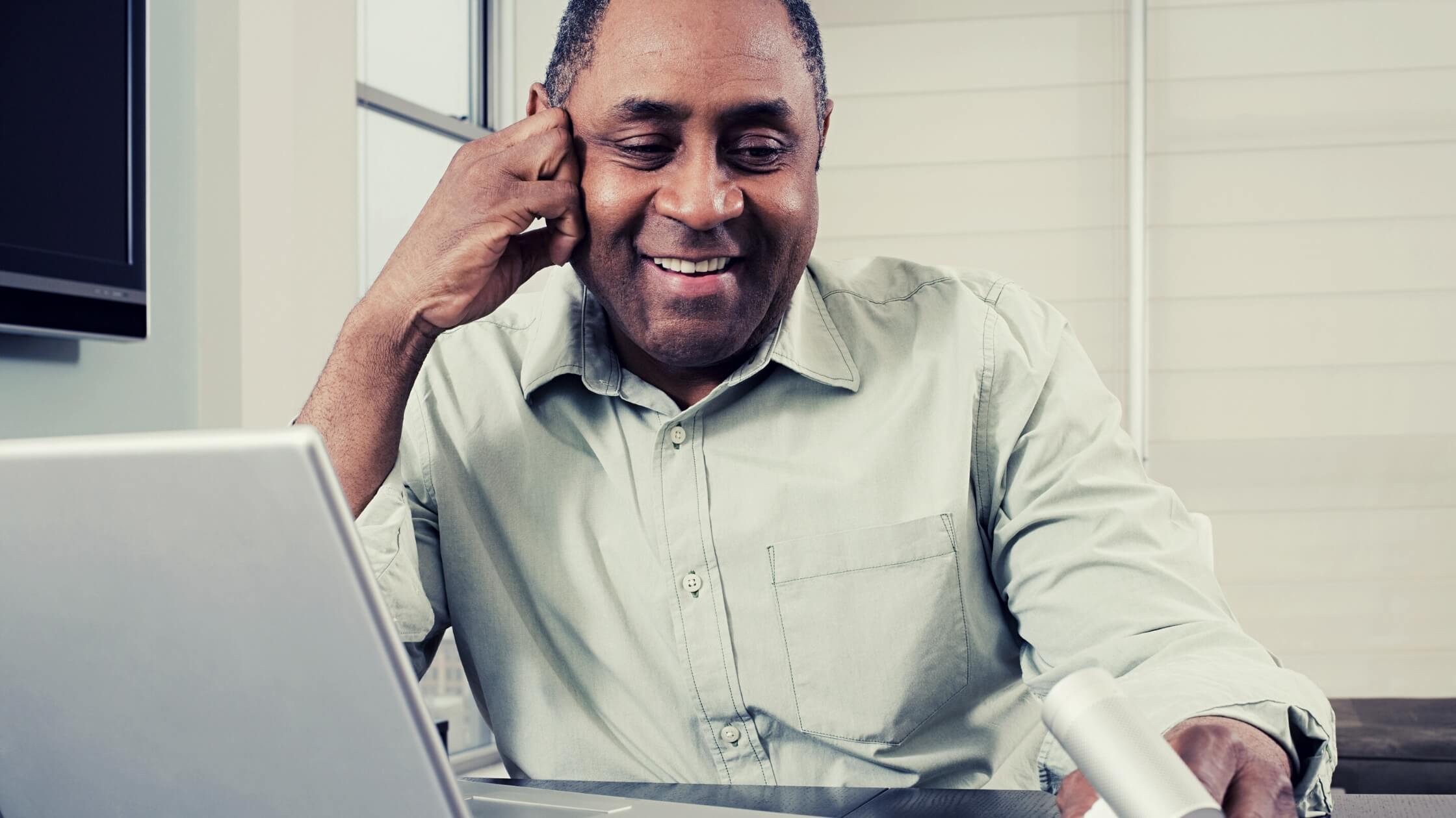 Hombre adulto, piel morena, sonriendo y trabajando con su laptop