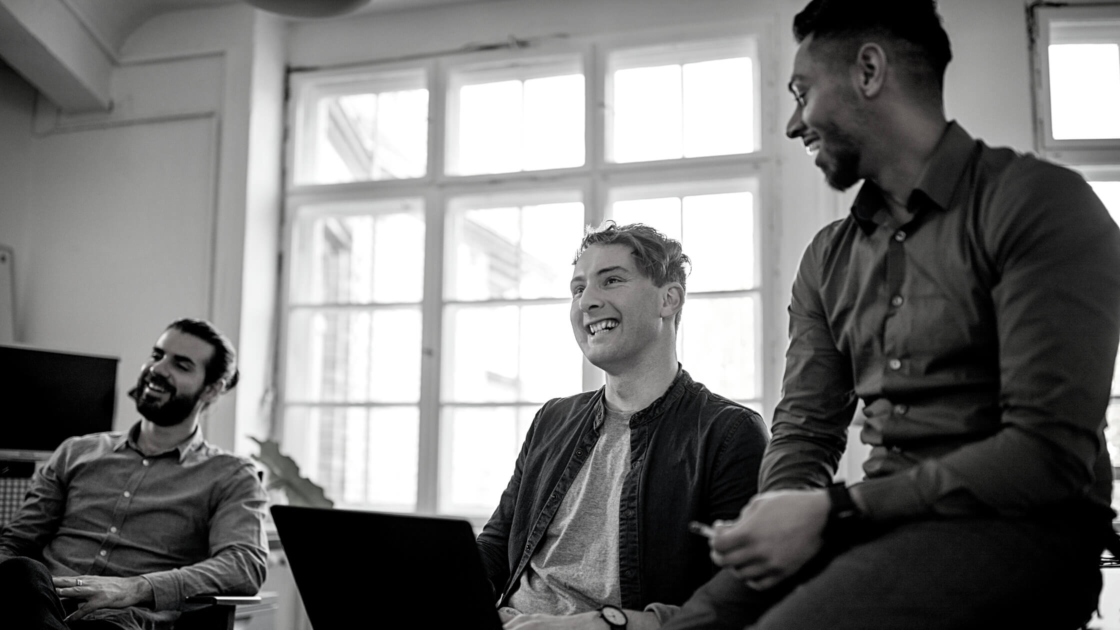 Grupo de hombres emprendedores conversando y sonriendo con sus laptops
