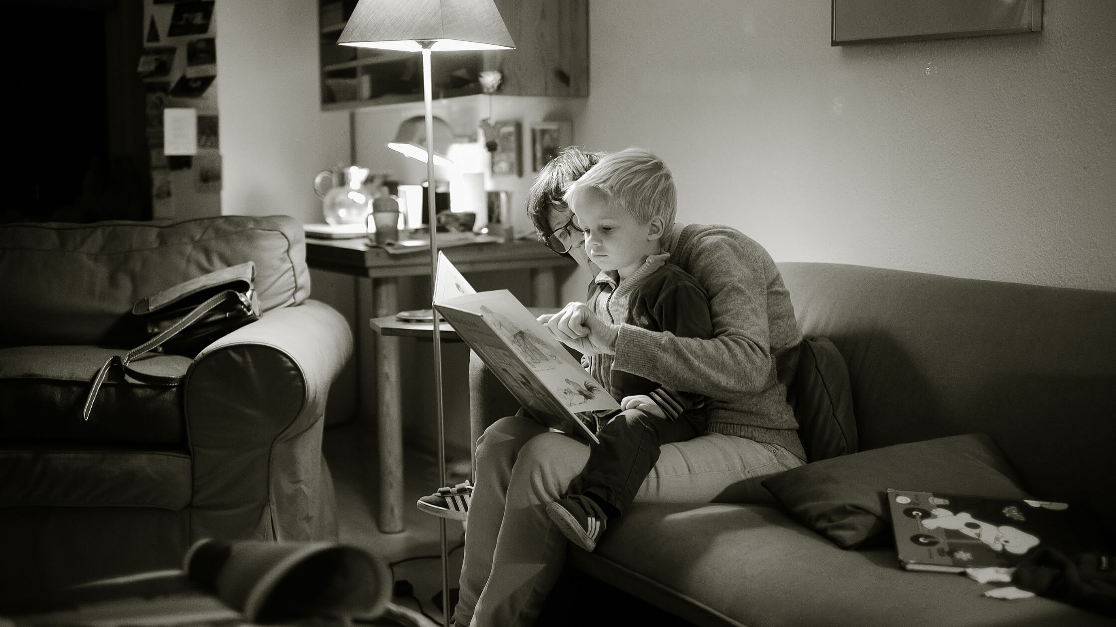 Mujer con lentes de unos 40 años en la sala de su casa, leyendo un libro a su hijo pequeño