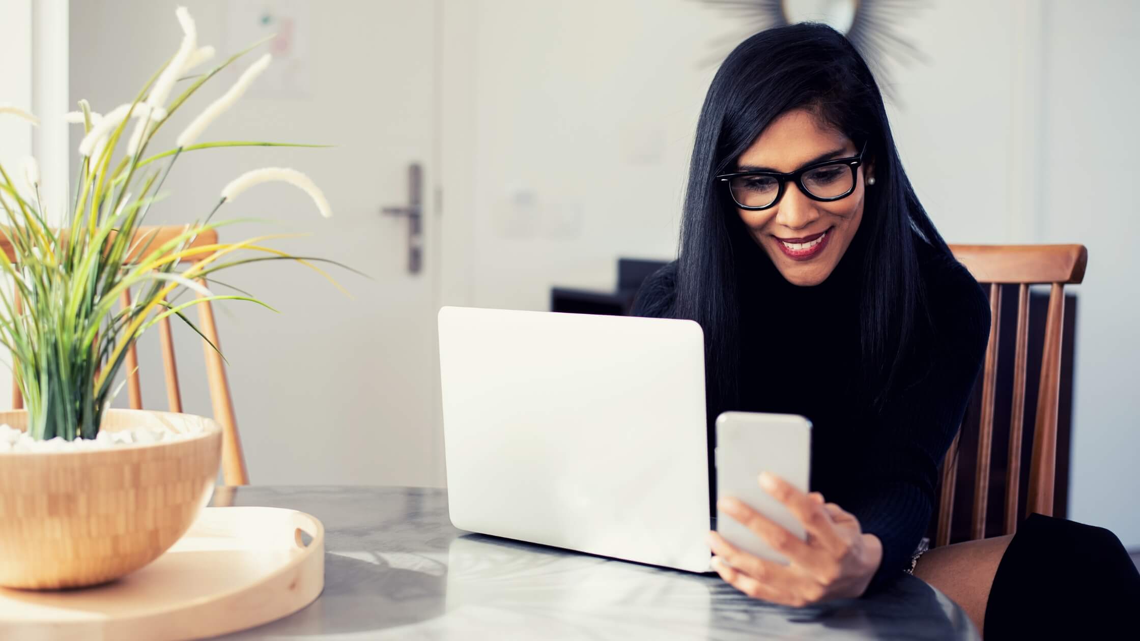Mujer emprendedora hispana, con lentes, con una laptop y un celular