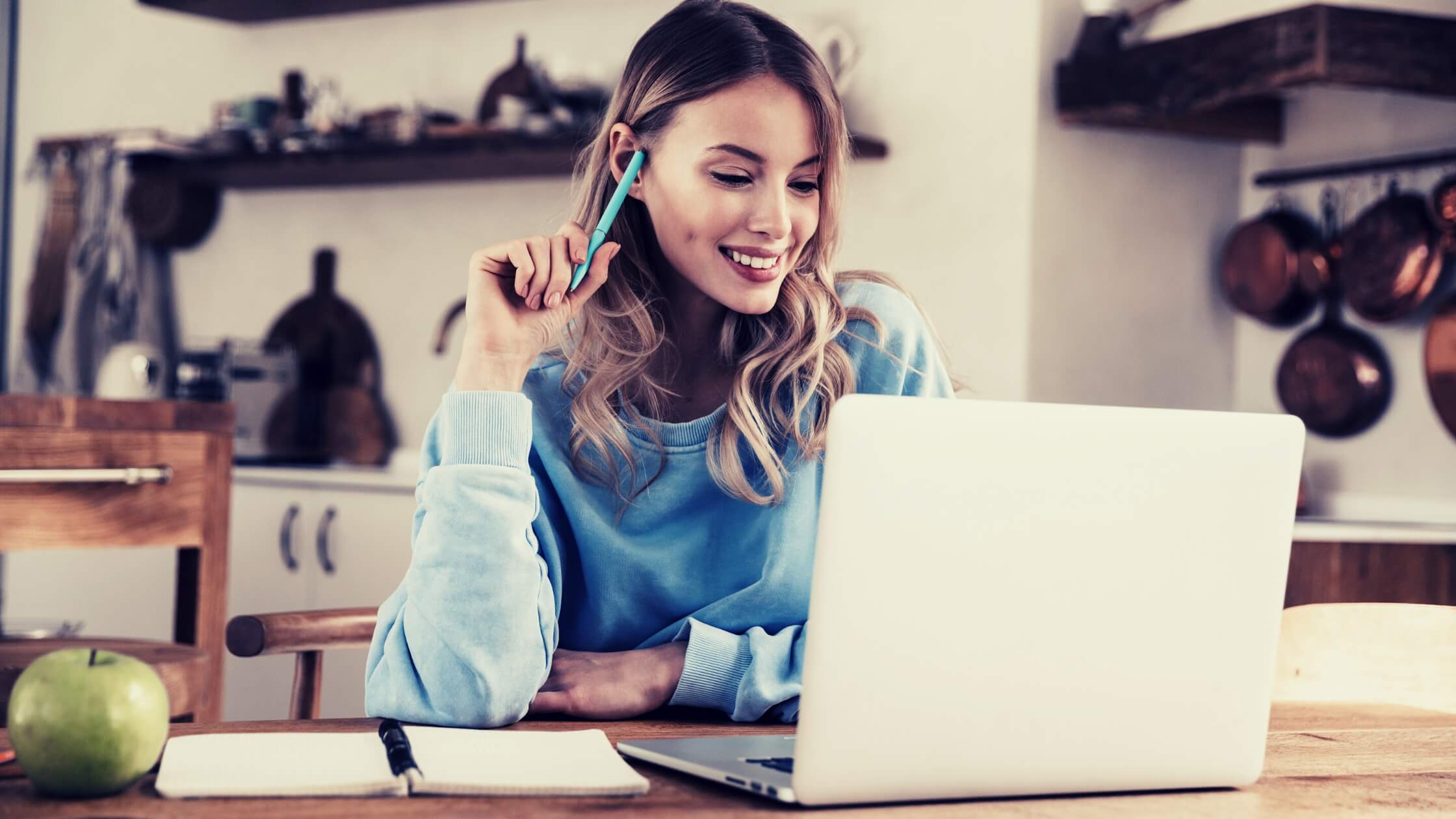 Mujer joven sonriente, freelancer, trabajando desde casa mirando a su laptop