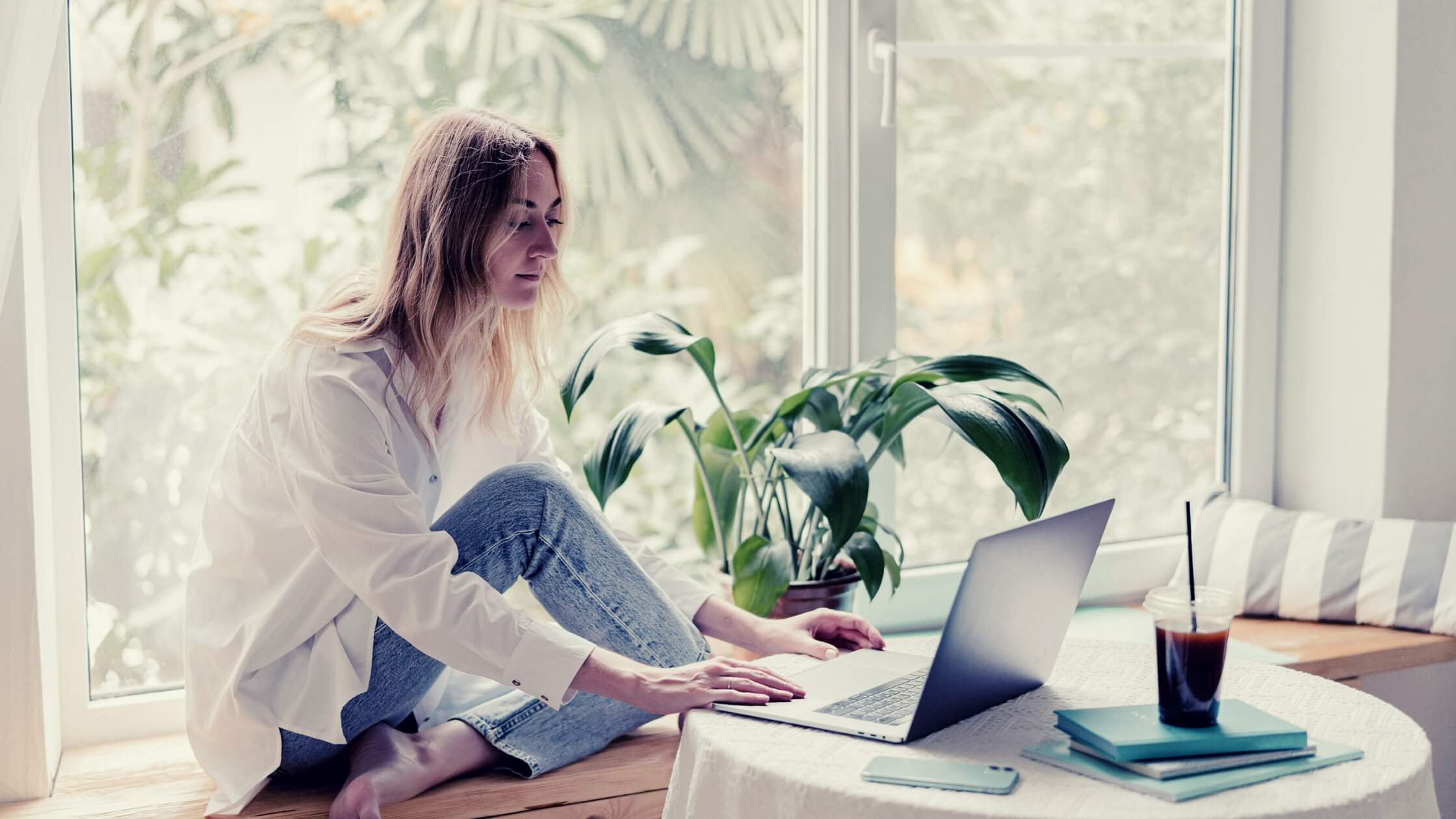 Mujer trabajando con su laptop desde su casa, con una planta artificial y un ambiente minimalista