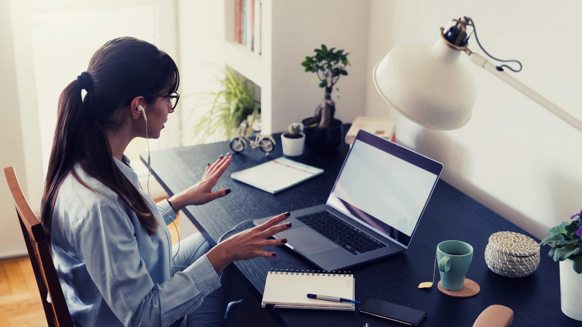 Mujer joven sonriente, freelancer, con lentes y audifonos teniendo una video llamada con su laptop, desde casa