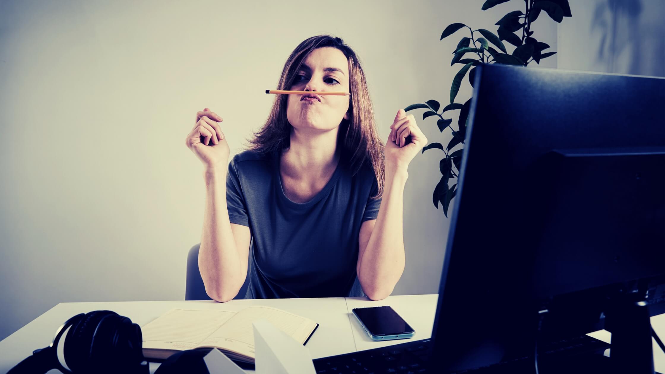 Mujer joven, trabajando de forma remota en su oficina distraída jugando con un lapiz en su boca