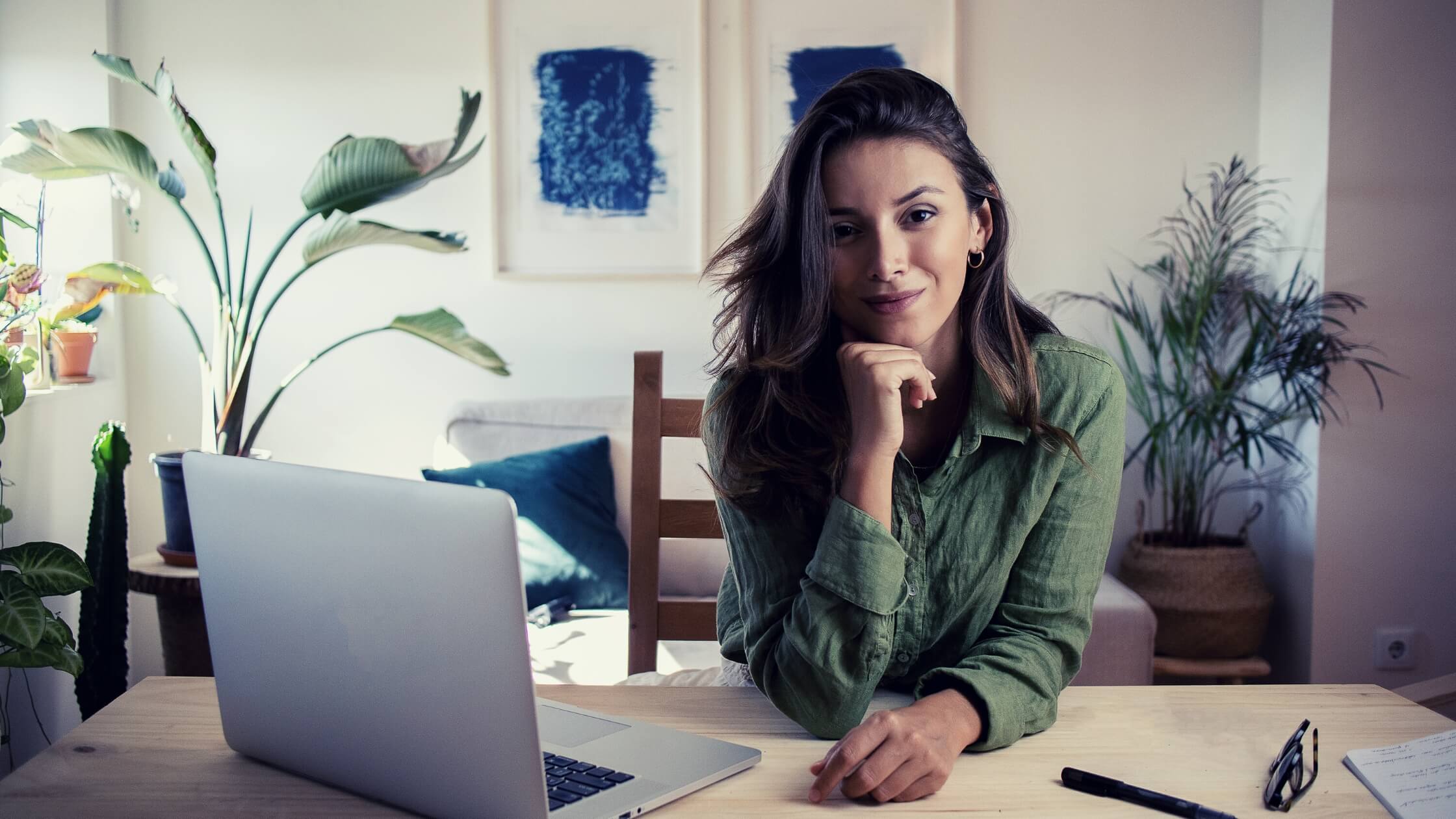 Mujer emprendedora de sweater verde trabajando desde casa con su laptop