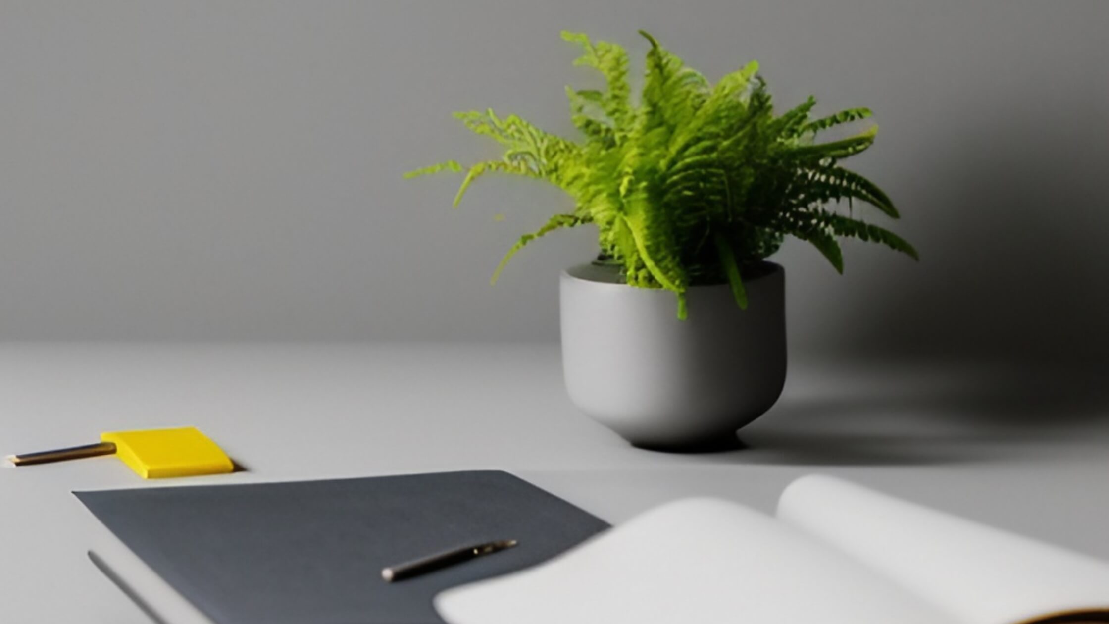 Un escritorio con una planta artificial en un matero gris y unos cuadernos y agendas